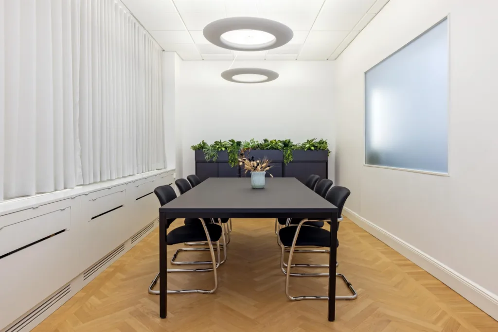 4. Ett konferensrum med svart bord, svarta stolar och växter längs väggen.
