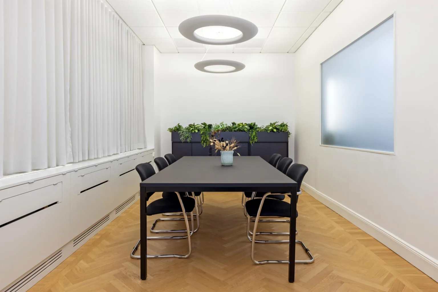 4. Ett konferensrum med svart bord, svarta stolar och växter längs väggen.