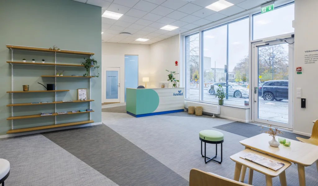 5. Ett väntrum med reception, hyllor, sittplatser och stora fönster som vetter ut mot en gata.