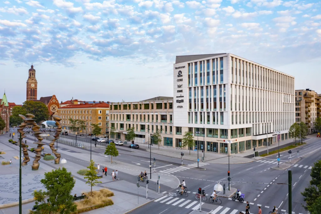 En modern stadsbyggnad i flera våningar med stora fönster och en öppen gata med övergångsställen framför.