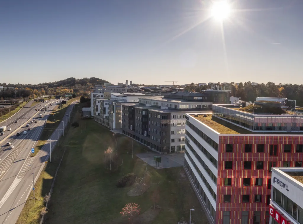 En vy över ett område med moderna byggnader, grönområden och solig himmel.