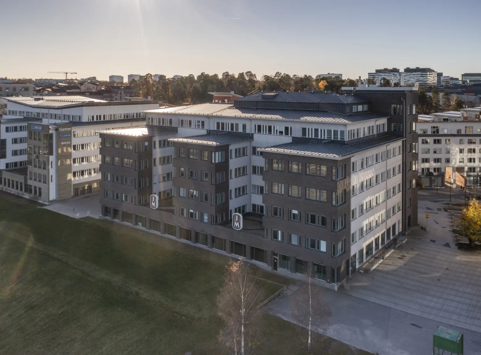 Ett flervåningshus med mörk fasad, omgiven av grön mark under en klar himmel.