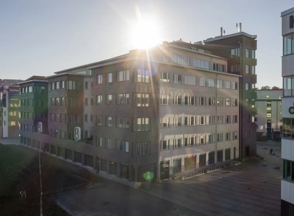 En byggnad med glas- och betongfasad, där solen strålar över taket och skapar ett starkt ljusflöde.