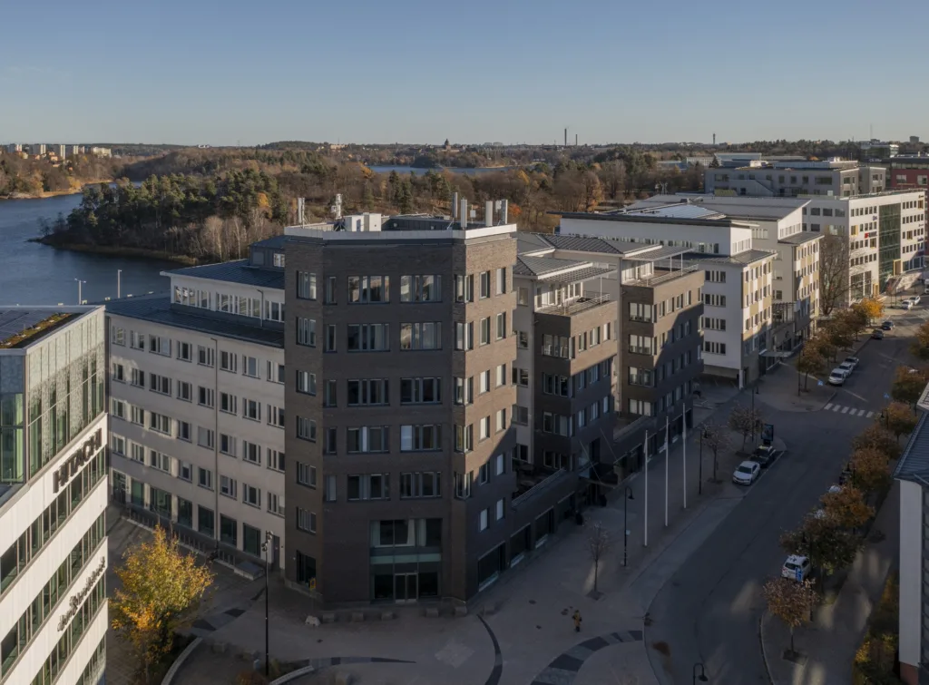 En rad moderna byggnader i en stadsdel, med asfaltvägar och höstfärgade träd i förgrunden.