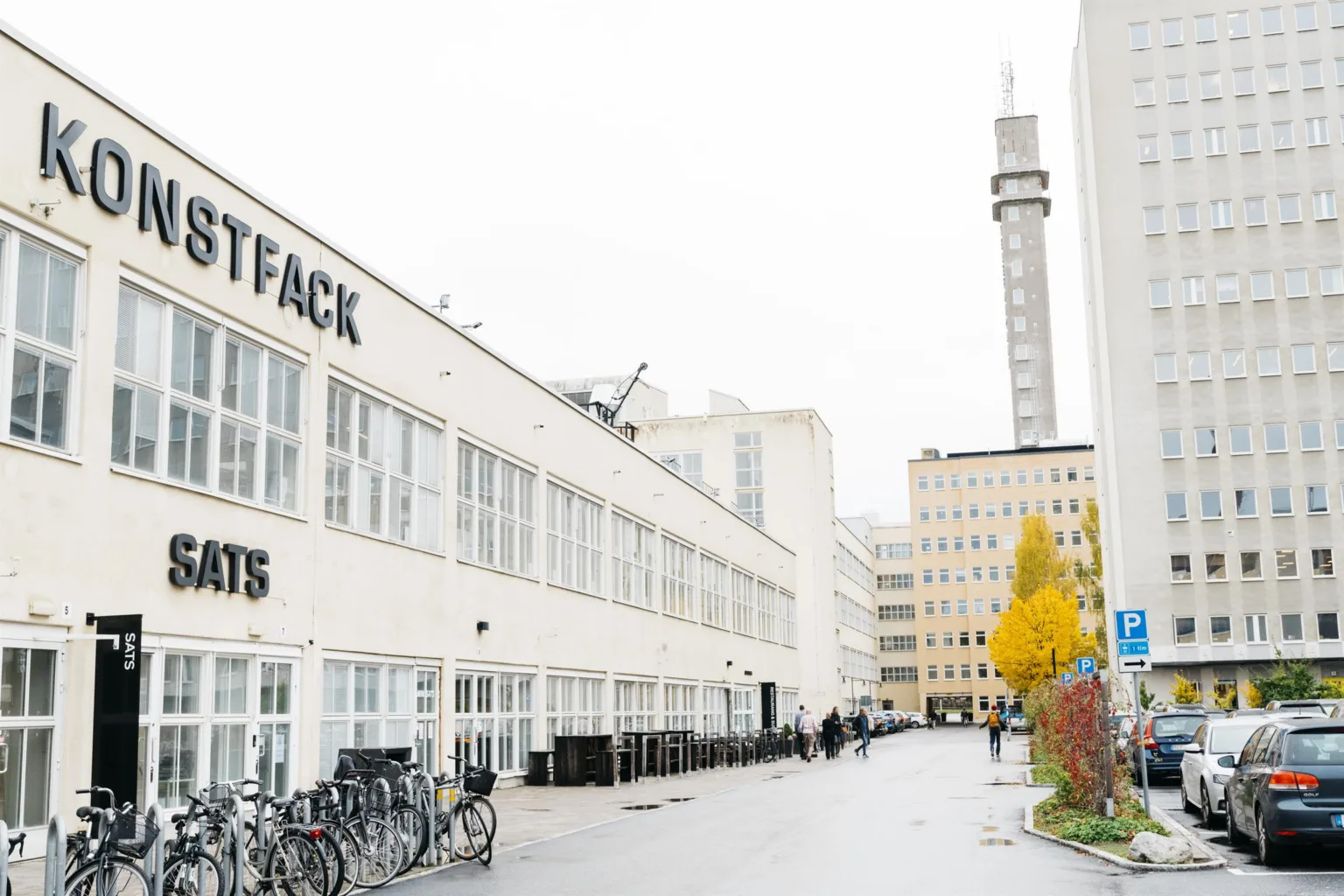 En vit byggnad med texten "STOCKHOLMS KONSTFACK" på fasaden, cyklar parkerade längs vägen och en tornliknande byggnad i bakgrunden.