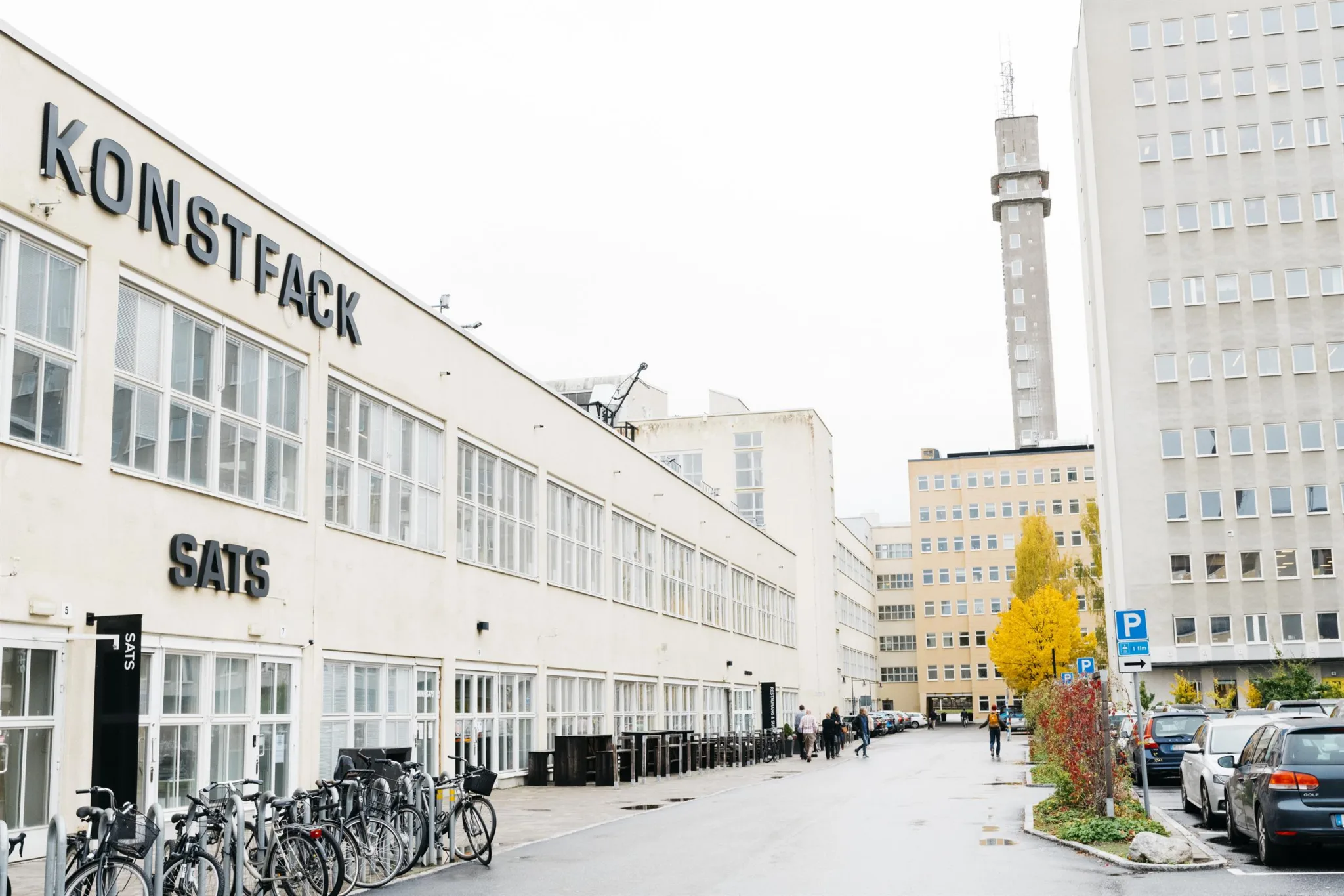 En vit byggnad med texten "STOCKHOLMS KONSTFACK" på fasaden, cyklar parkerade längs vägen och en tornliknande byggnad i bakgrunden.