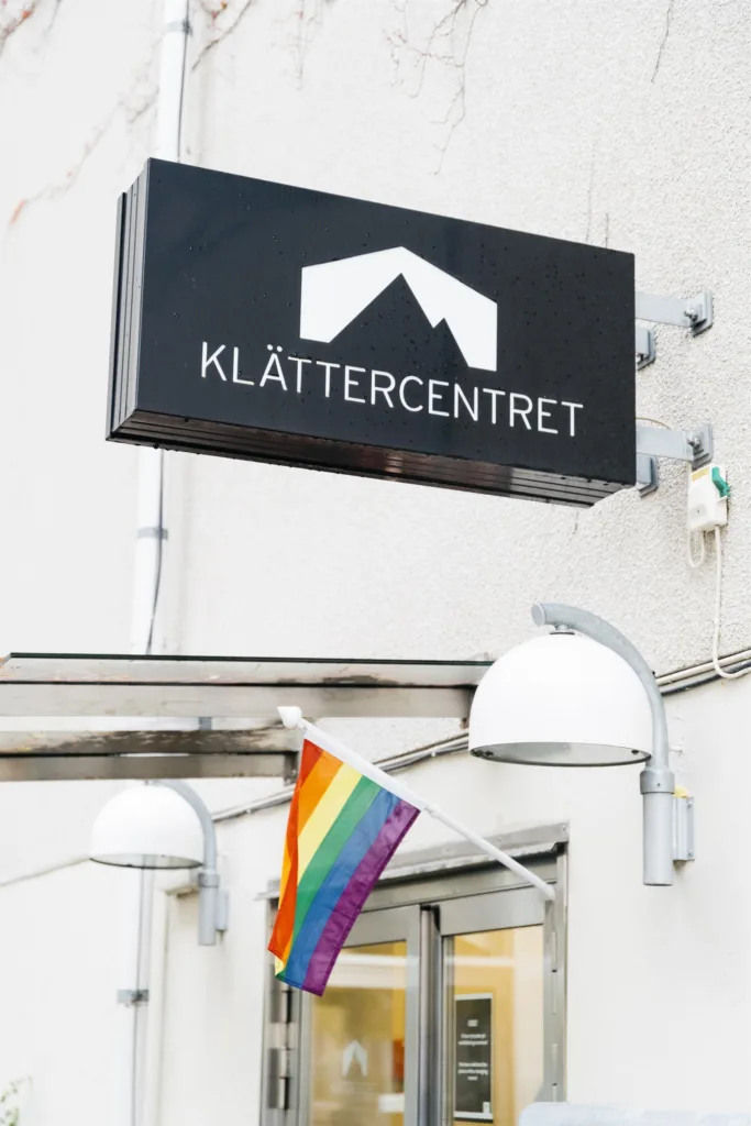 En skylt med texten "KLÄTTERCENTRET" ovanför en regnbågsflagga som hänger vid byggnaden.