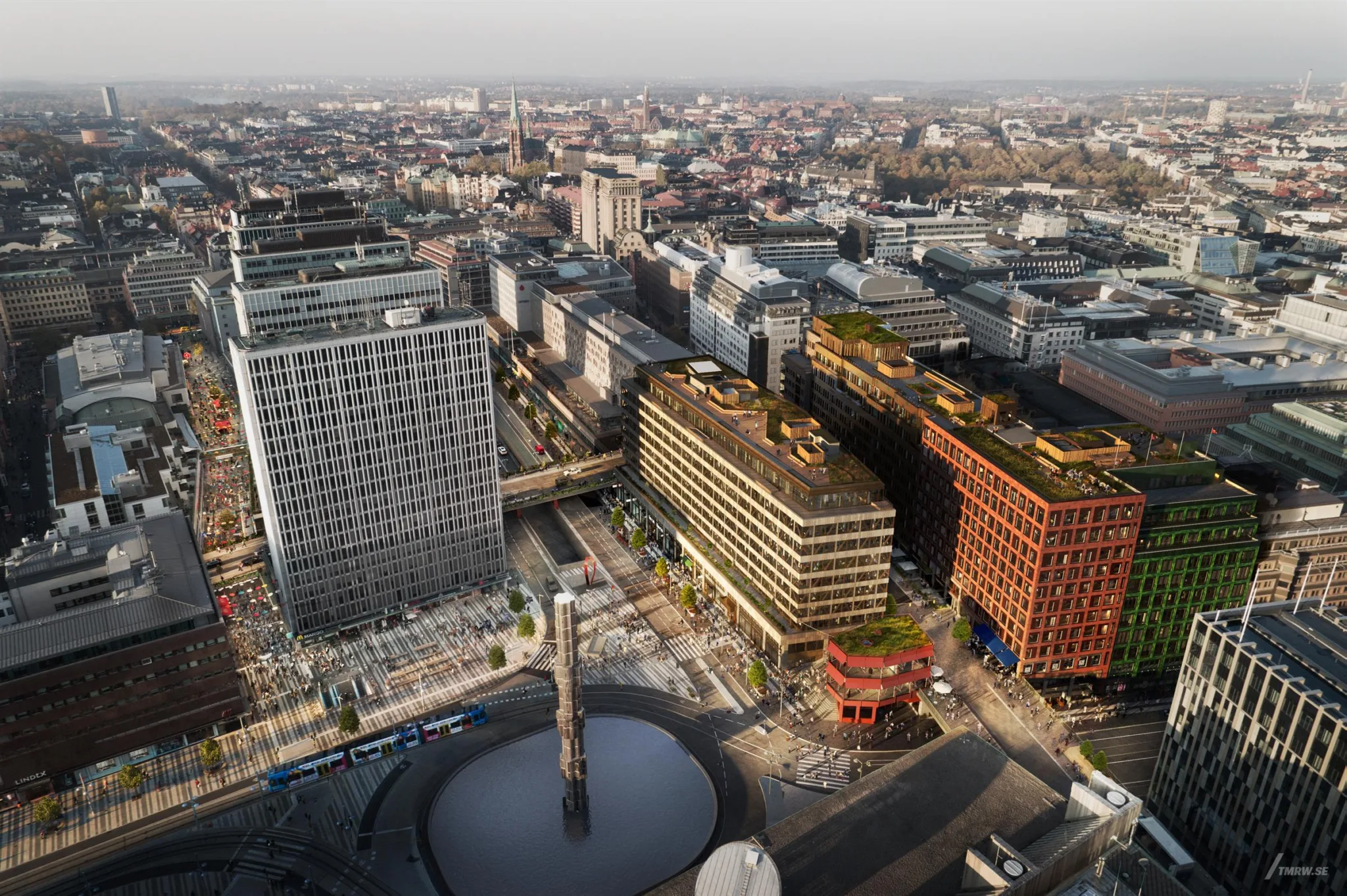 En stadsbild med flera byggnader, gröna tak och en fontän i förgrunden.
