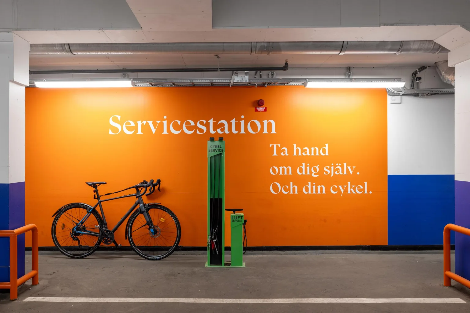 En cykelservicestation i ett garage med en orange vägg med texten: "Servicestation. Ta hand om dig själv. Och din cykel."