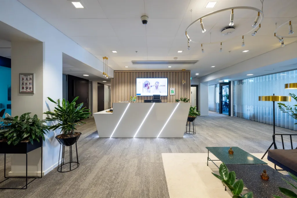 Reception med modern inredning, växter och en stor skärm på väggen.