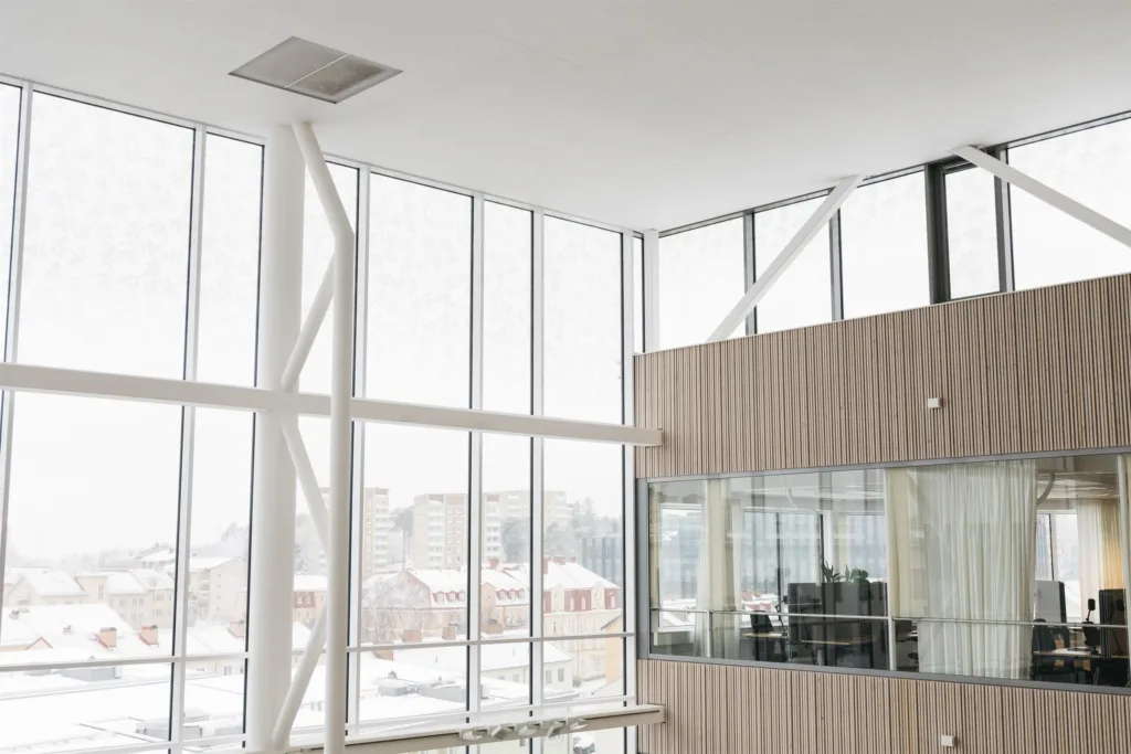 Interiör med stora glasfönster som släpper in mycket ljus, med utsikt över snöiga byggnader utanför.