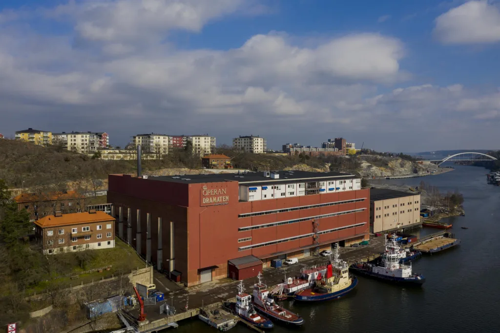 En stor röd tegelbyggnad vid en hamn, omgiven av båtar och stadsbebyggelse.