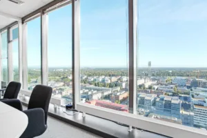 Ett rum med stora fönster som visar en panoramautsikt över en stad med byggnader och grönska.
