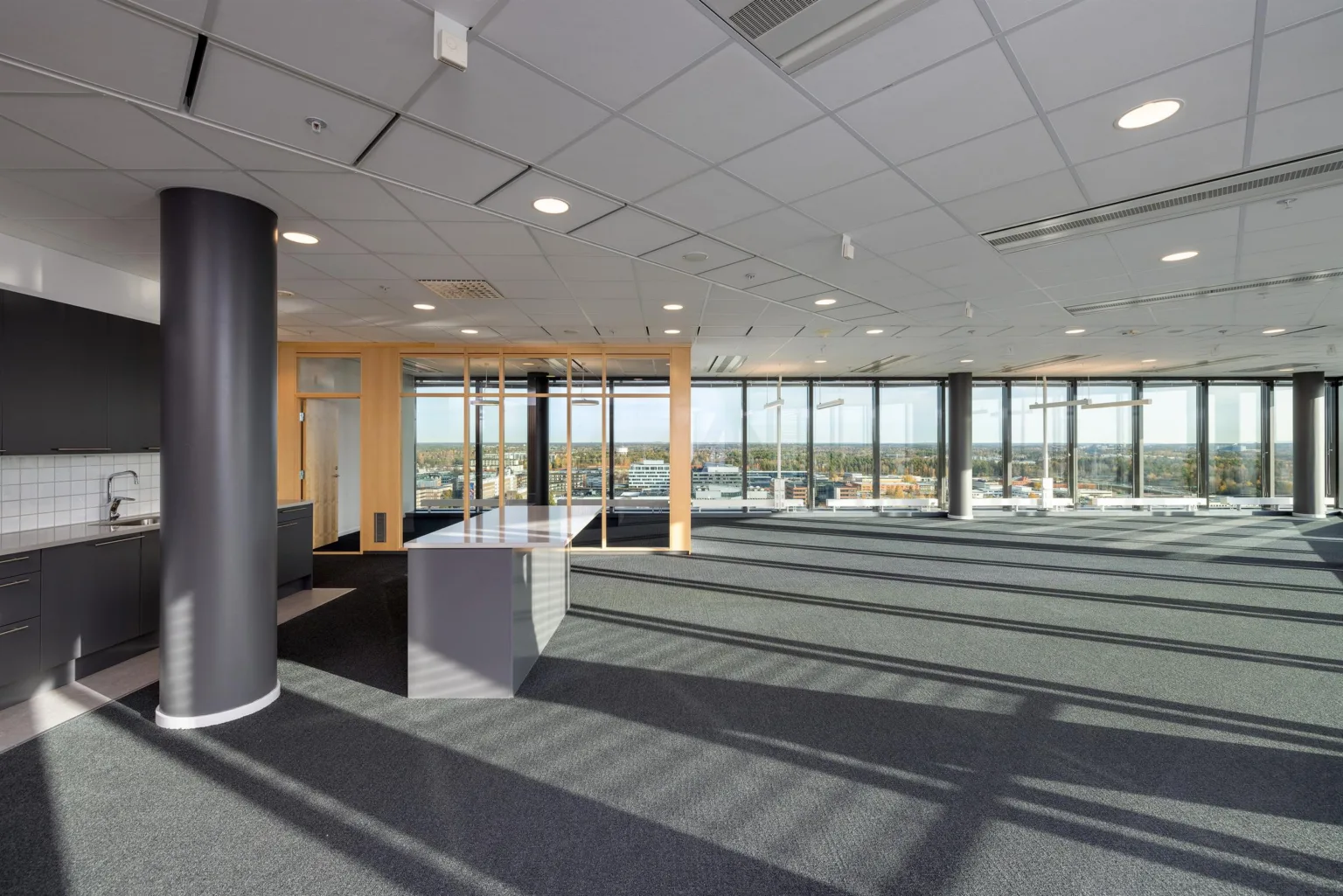Ett öppet kontorsutrymme med mattbeläggning, stora fönster och en reception eller arbetsyta vid sidan.