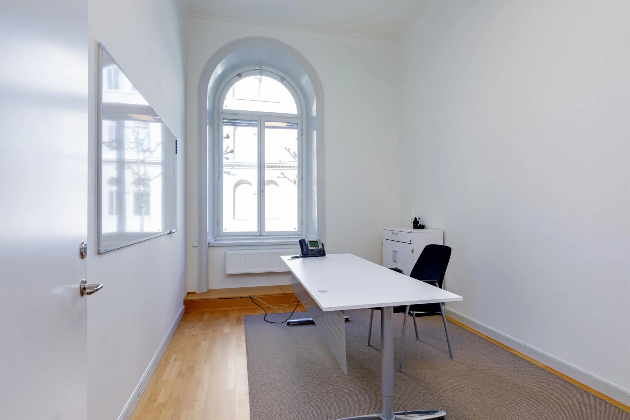 Ett litet kontor med ett skrivbord, en svart stol, en telefon och ett stort fönster.