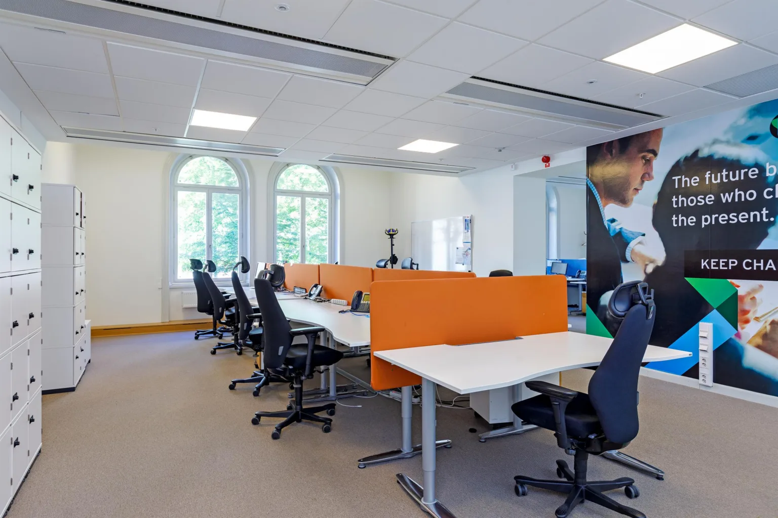 Ett kontor med skrivbord och orange avskärmningar, samt svarta kontorsstolar.