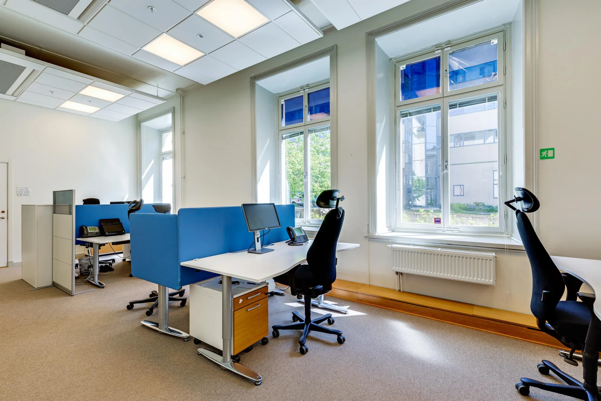 Ett kontor med arbetsstationer utrustade med blå avskärmningsväggar, svarta stolar och stora fönster med utsikt.
