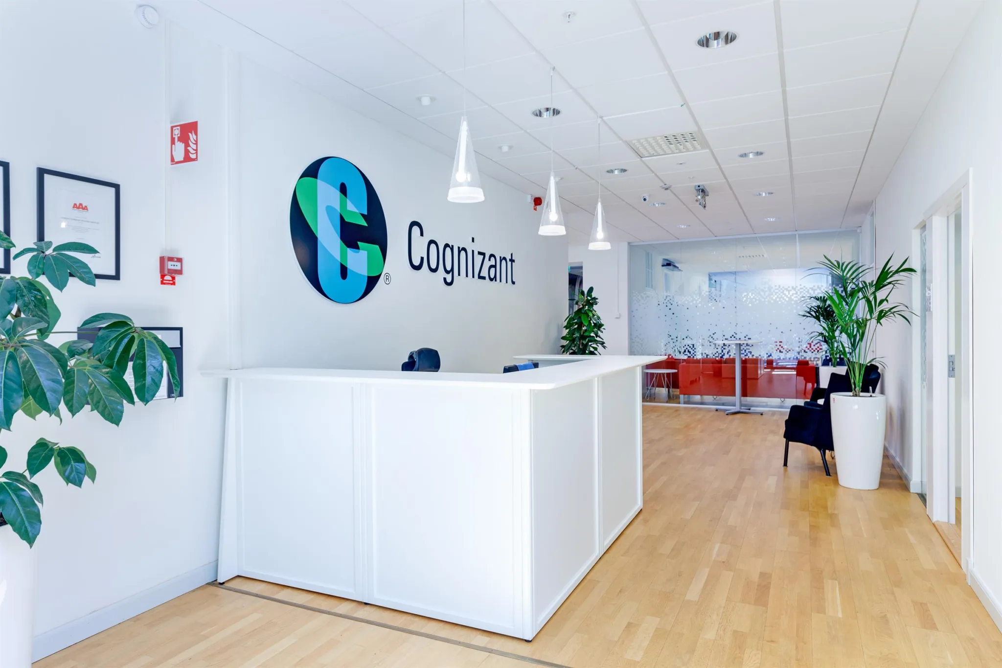 Reception med Cognizant-logotyp på väggen, vitt skrivbord, hängande lampor och trägolv.