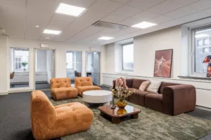 1. En lounge med bruna och orangea fåtöljer, ett soffbord, en brun soffa och dekorationer i ett ljust rum med tavlor på väggarna.