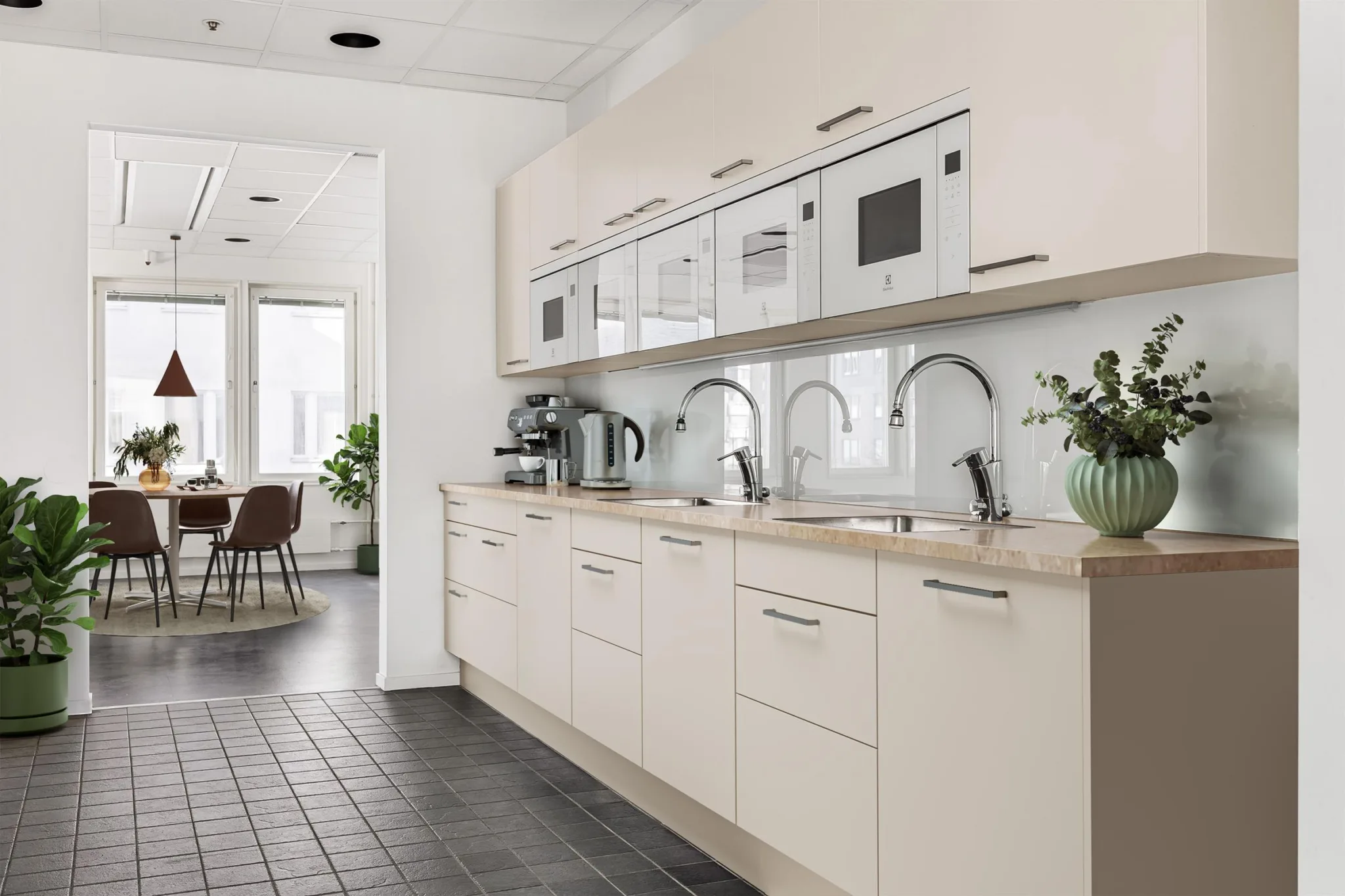 5. Ett modernt kök med ljusa skåp, flera kranar, och en kaffemaskin, med ett matbord synligt i bakgrunden.