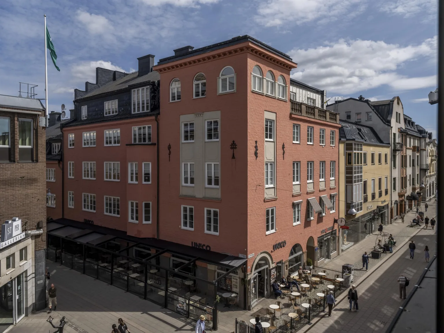 En större rosa byggnad med uteservering vid trottoaren och omgivande stadsmiljö.