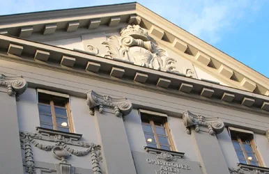 Fasad av en byggnad med dekorativa detaljer och fönster under en blå himmel.