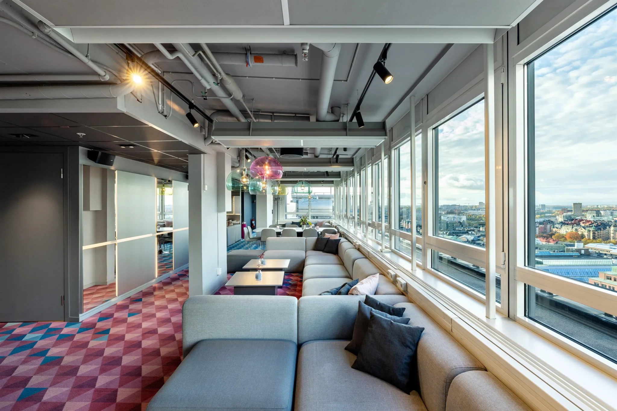 1. En lounge med grå soffor och kuddar i ett rum med stora fönster som ger utsikt över staden.