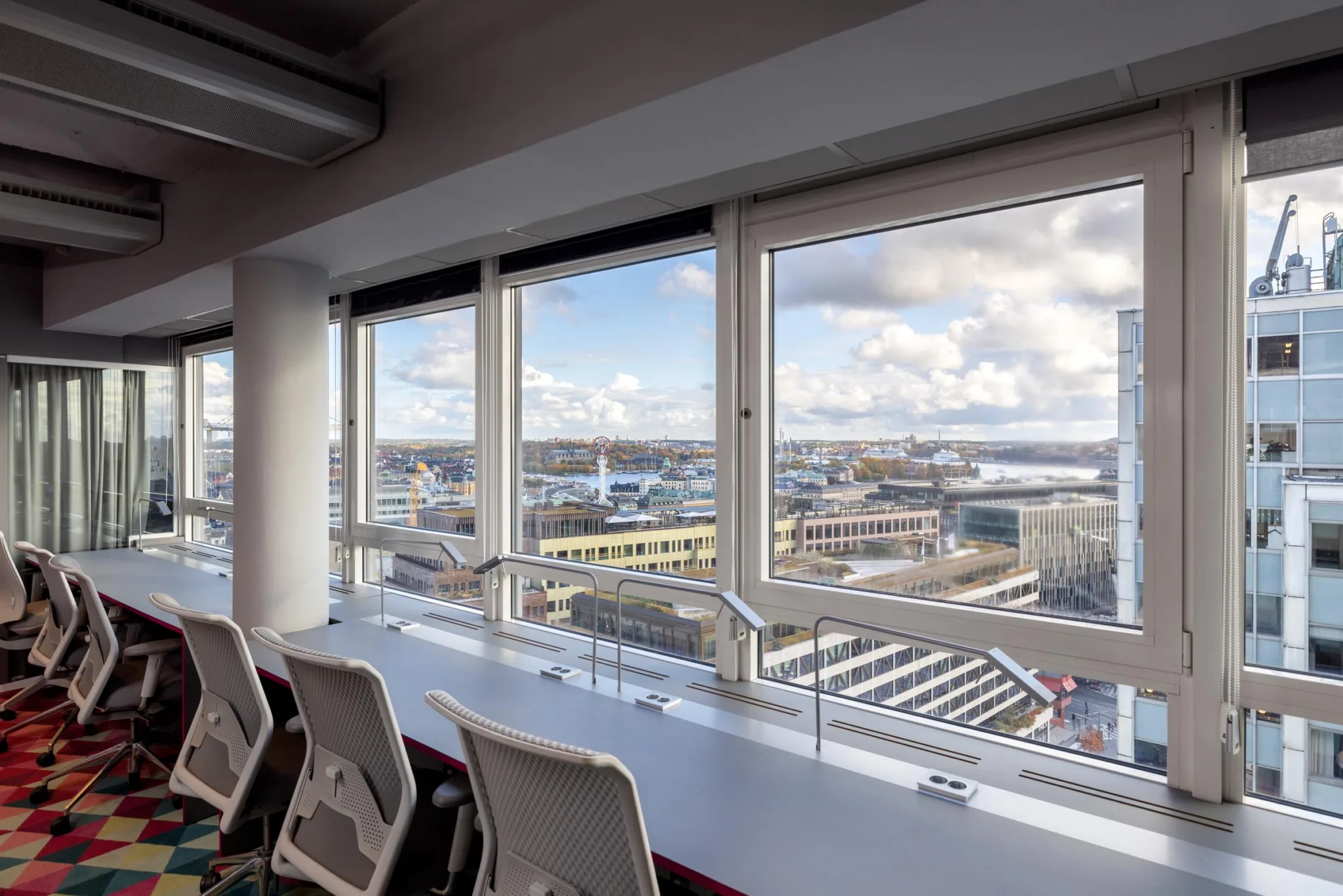 4. Ett rum med höga fönster som visar stadsvy och stolar placerade vid ett långt bord.