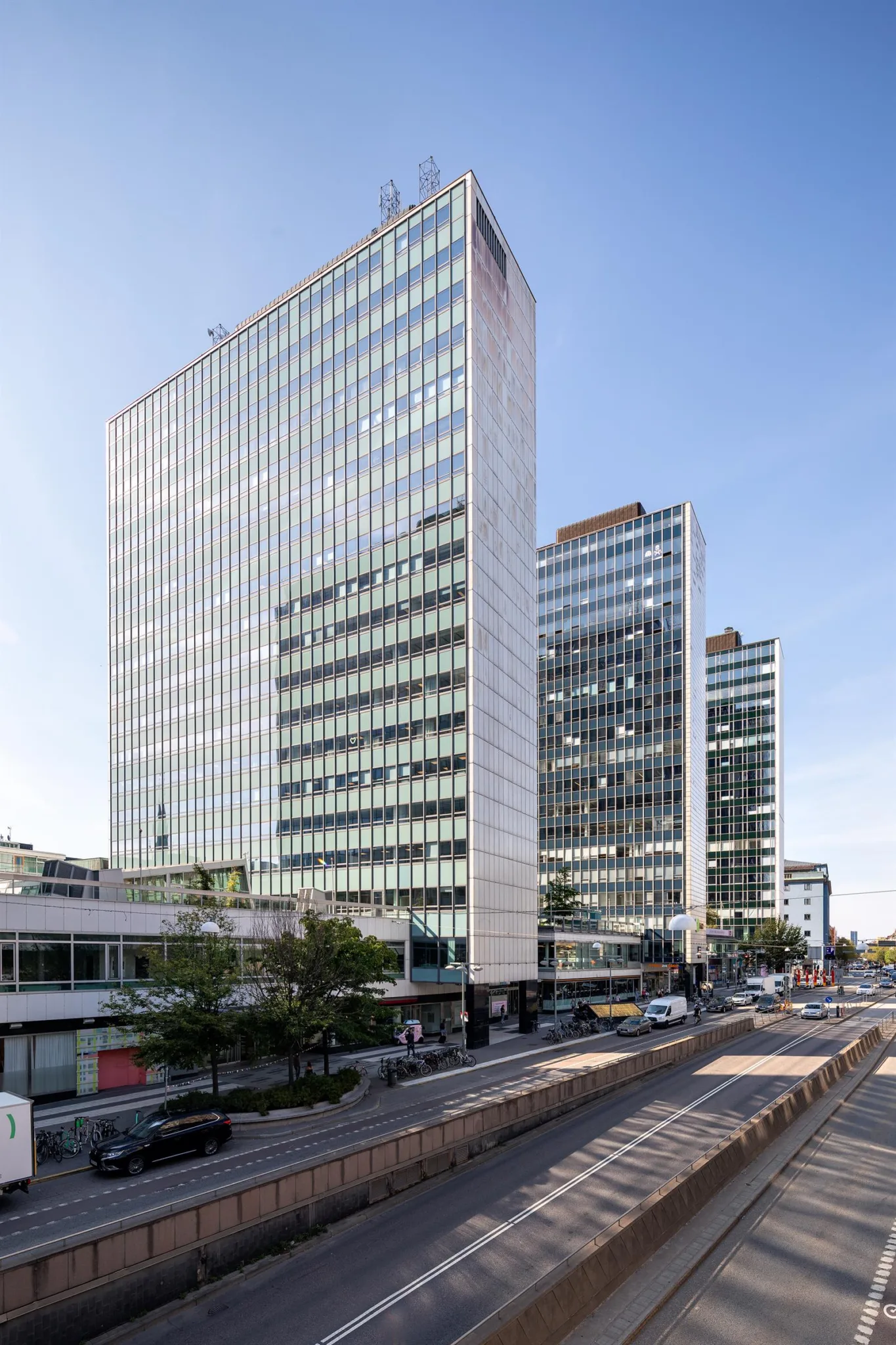 Höga kontorsbyggnader i glas och betong längs en stadsgata med trafik.