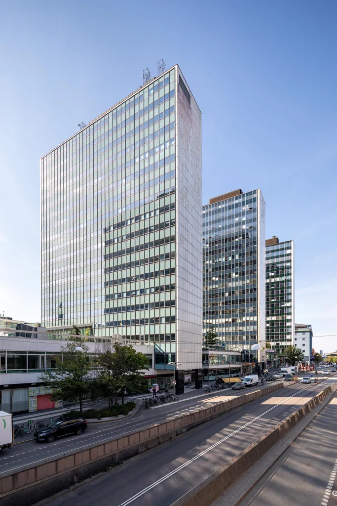 Höga kontorsbyggnader i glas och betong längs en stadsgata med trafik.