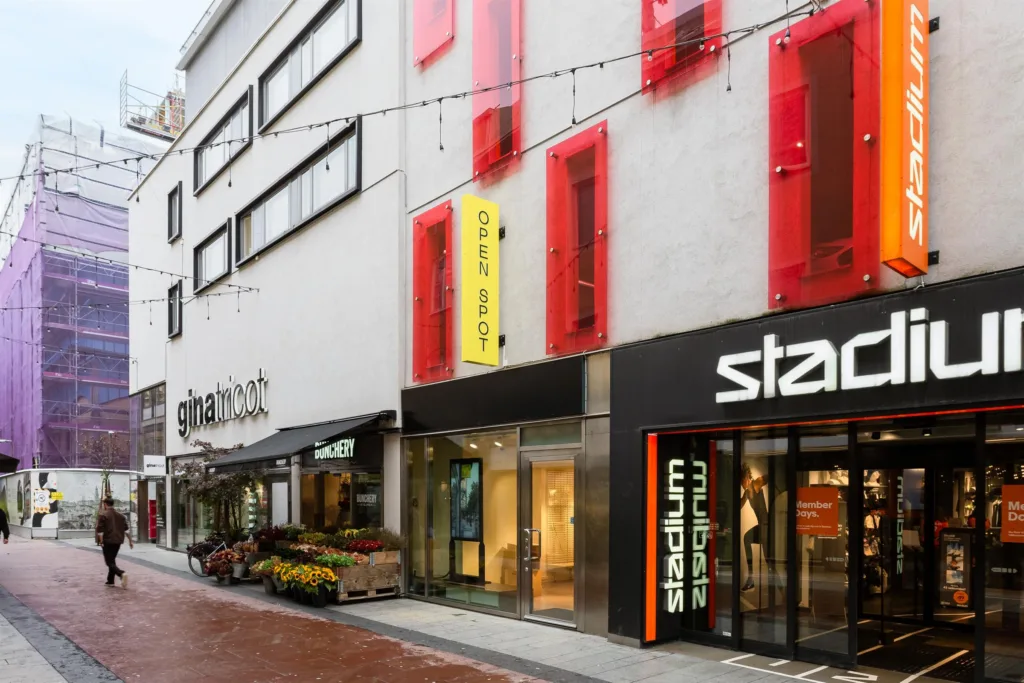 En byggnadsfasad med röda paneler, flera butiksingångar och texten "Stadium" synlig.