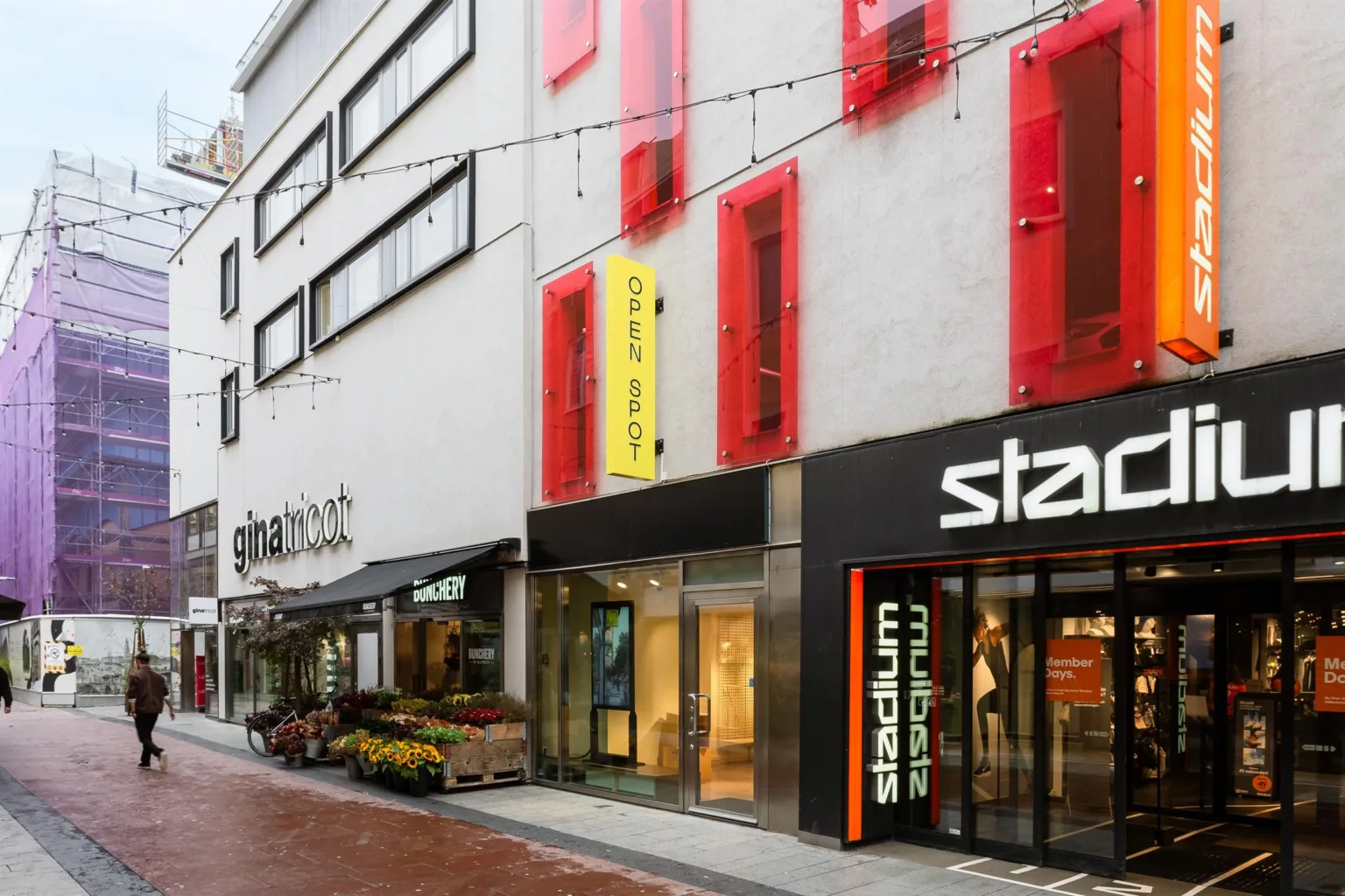 En byggnadsfasad med röda paneler, flera butiksingångar och texten "Stadium" synlig.
