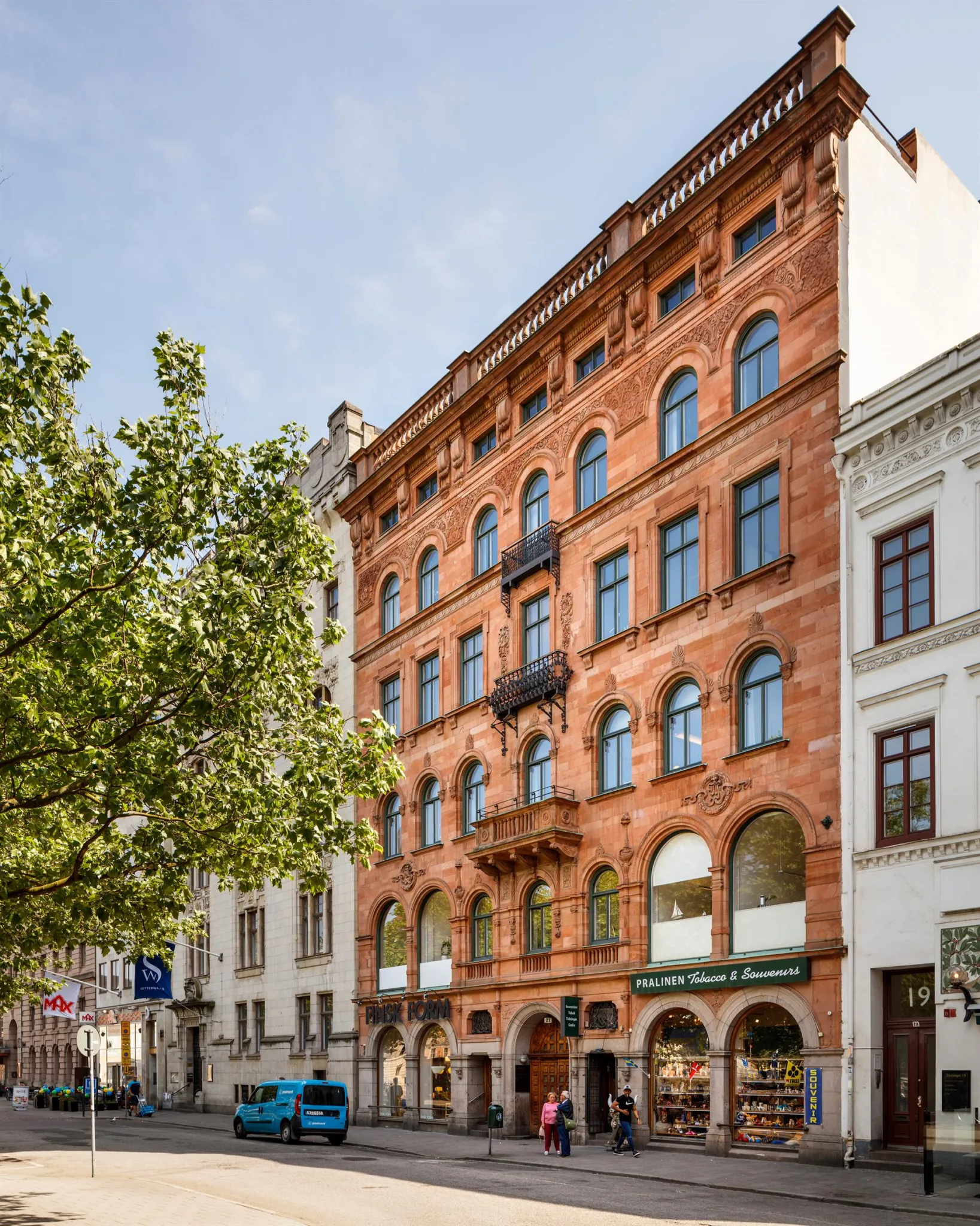3. En röd tegelbyggnad med flera våningar och bågformade fönster, omgiven av andra byggnader och grönska.