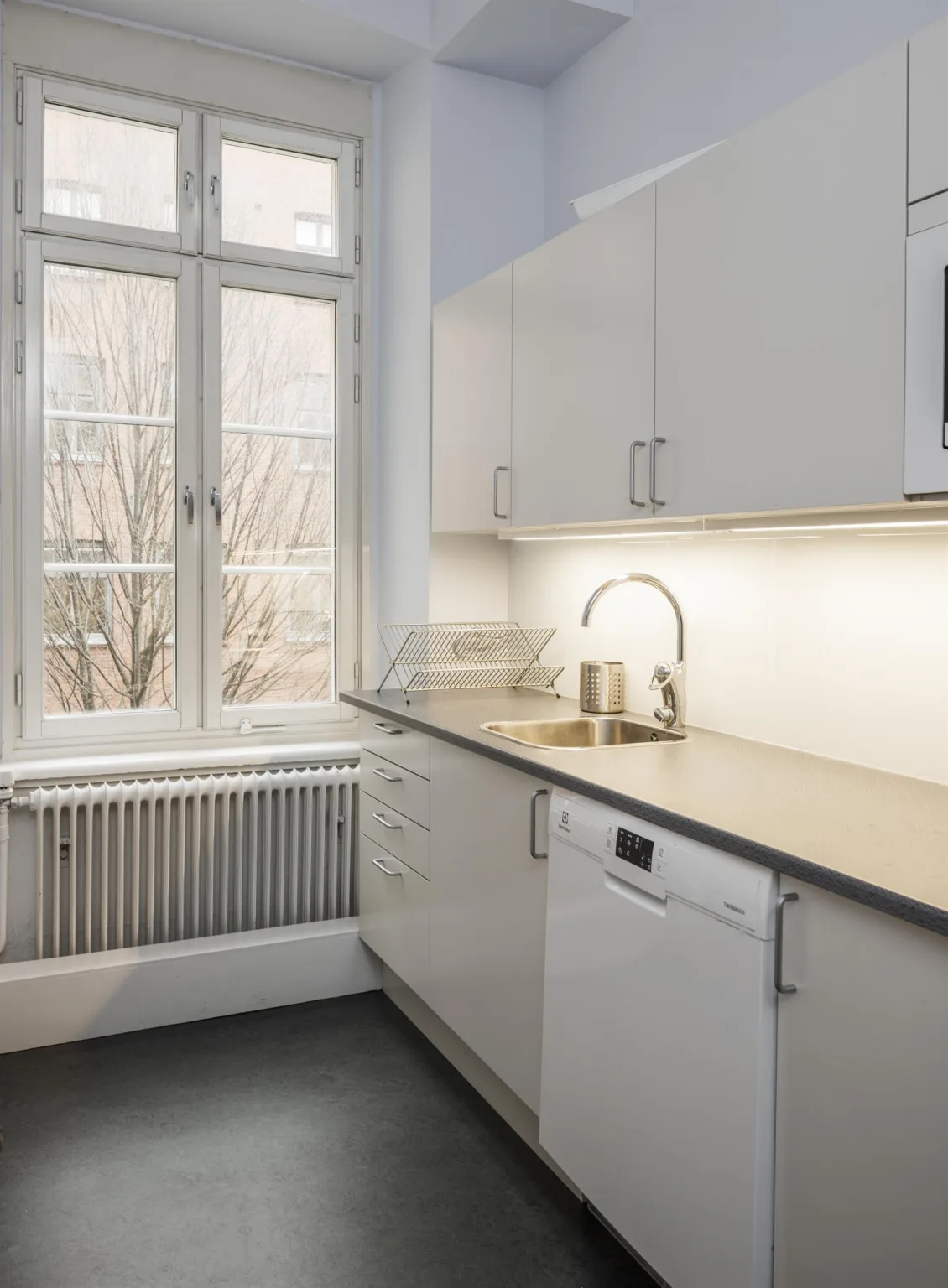 4. Ett kök med vita skåp, bänkskiva, diskho och ett fönster som släpper in dagsljus.