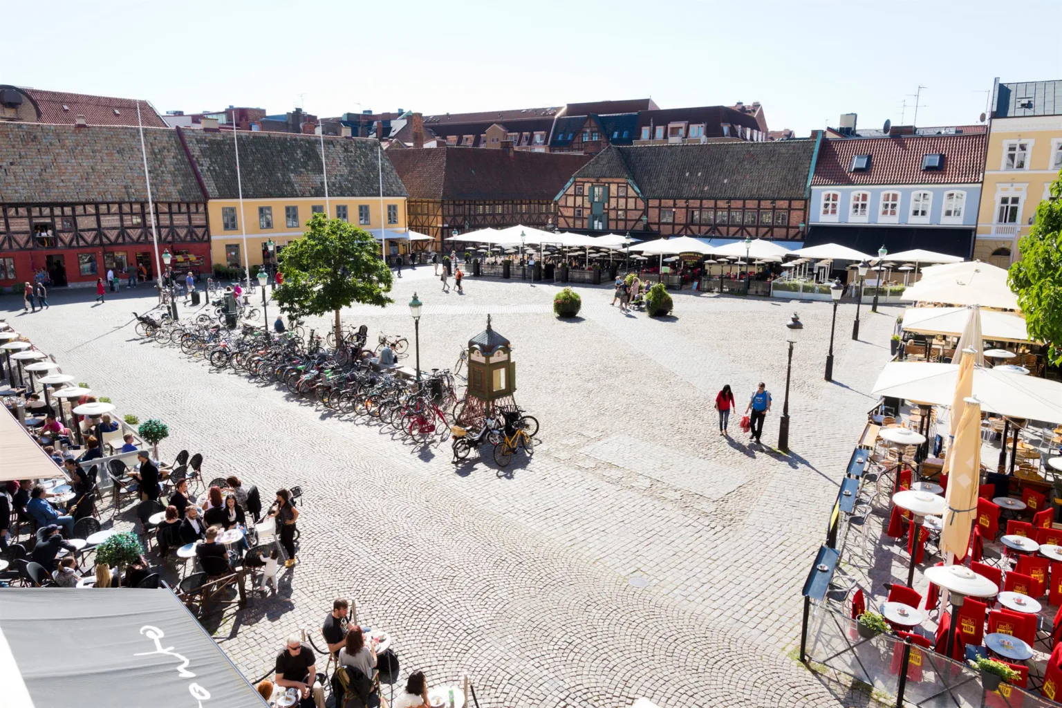 1. Ett torg med cyklar, en staty, uteserveringar och människor i en historisk stadsmiljö.