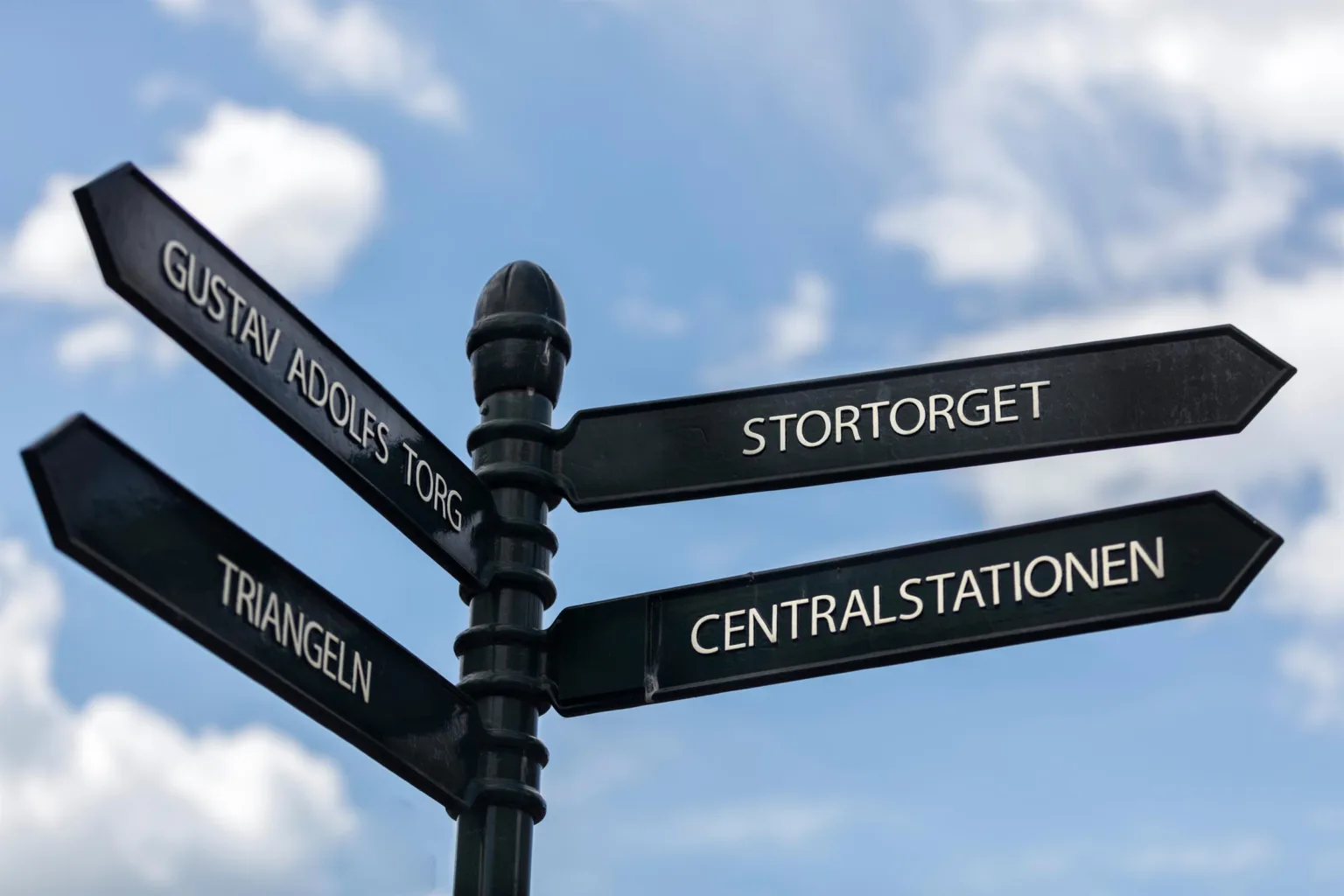 5. En svart skyltstolpe med riktningar, där texten "Stortorget", "Centralstationen" och "Triangeln" syns mot en blå himmel.