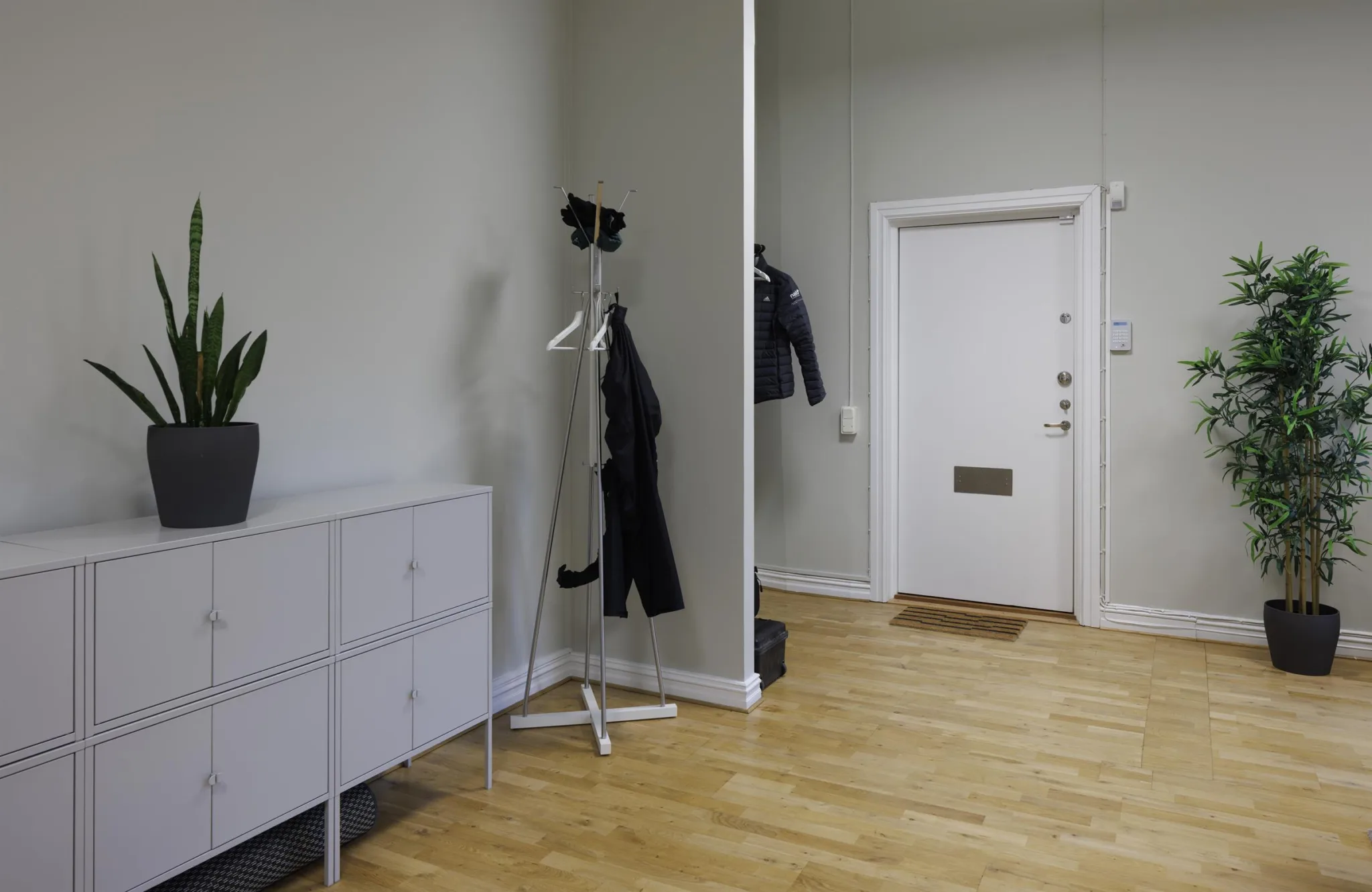 1. En hall med ett vitt skoskåp, en spegel och en klädhängare med jackor mot en ljus vägg.