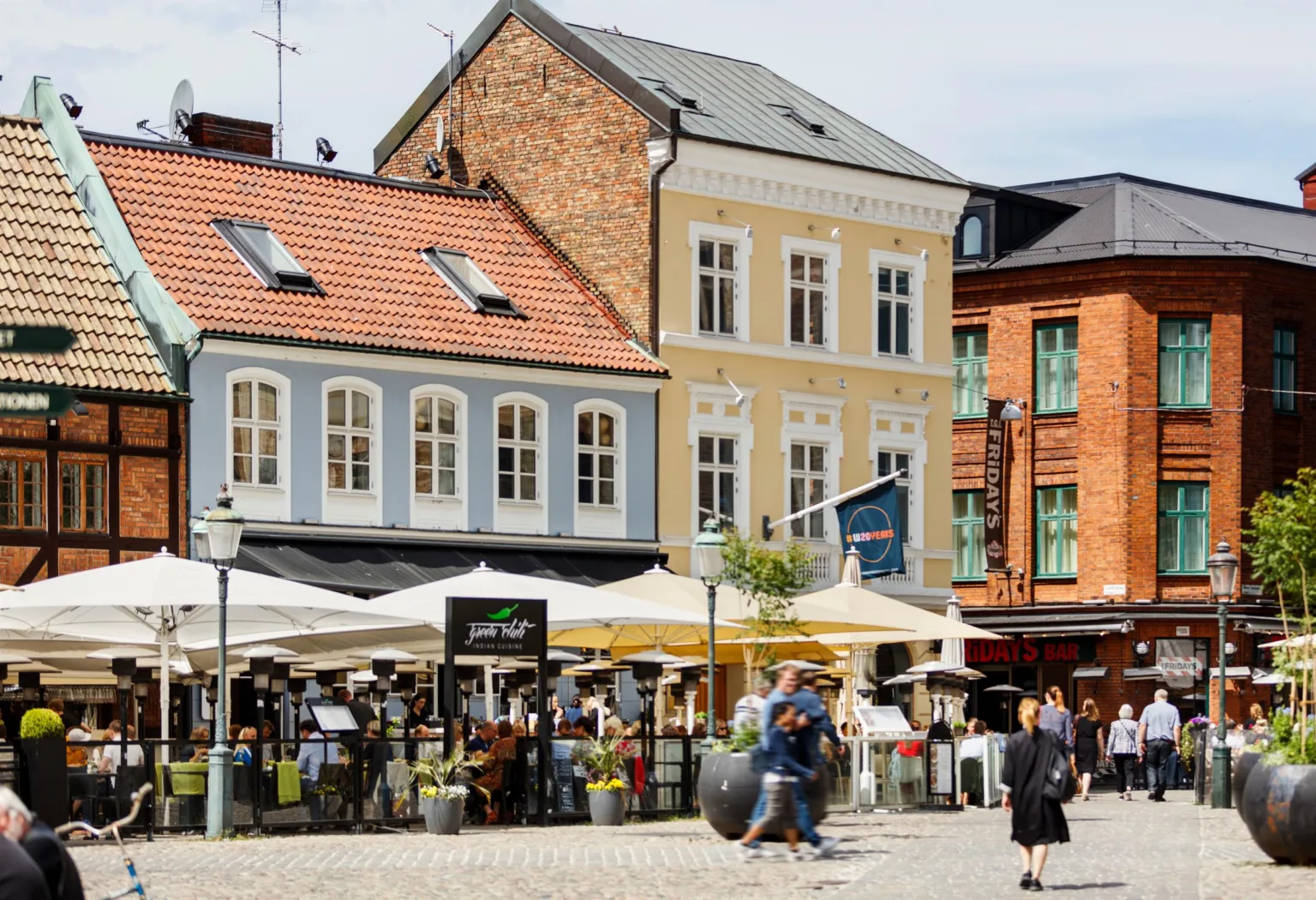 4. Ett torg med uteserveringar, människor som promenerar, och färgglada fasader på hus i bakgrunden.