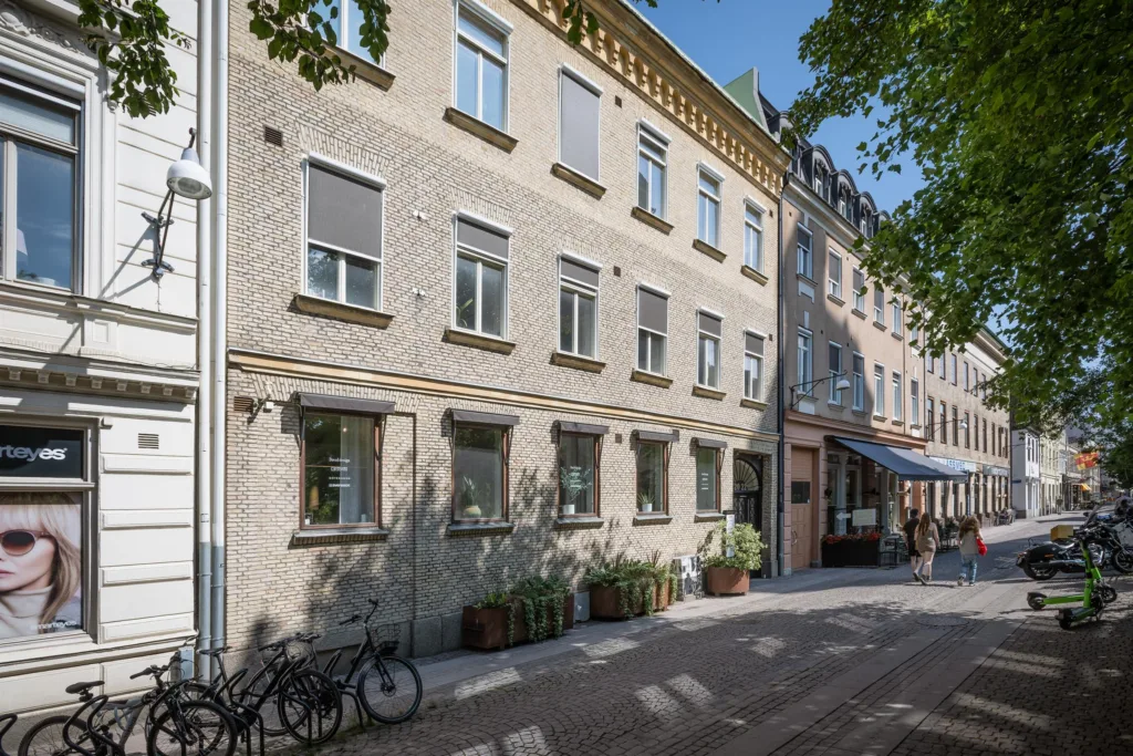Gata med tegelbyggnader, fönster och planterade krukväxter, samt cyklar parkerade längs fasaden.