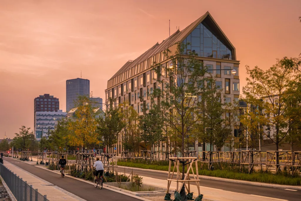 4. En byggnad med triangulärt tak, omgiven av träd och människor som promenerar under en orangefärgad himmel.