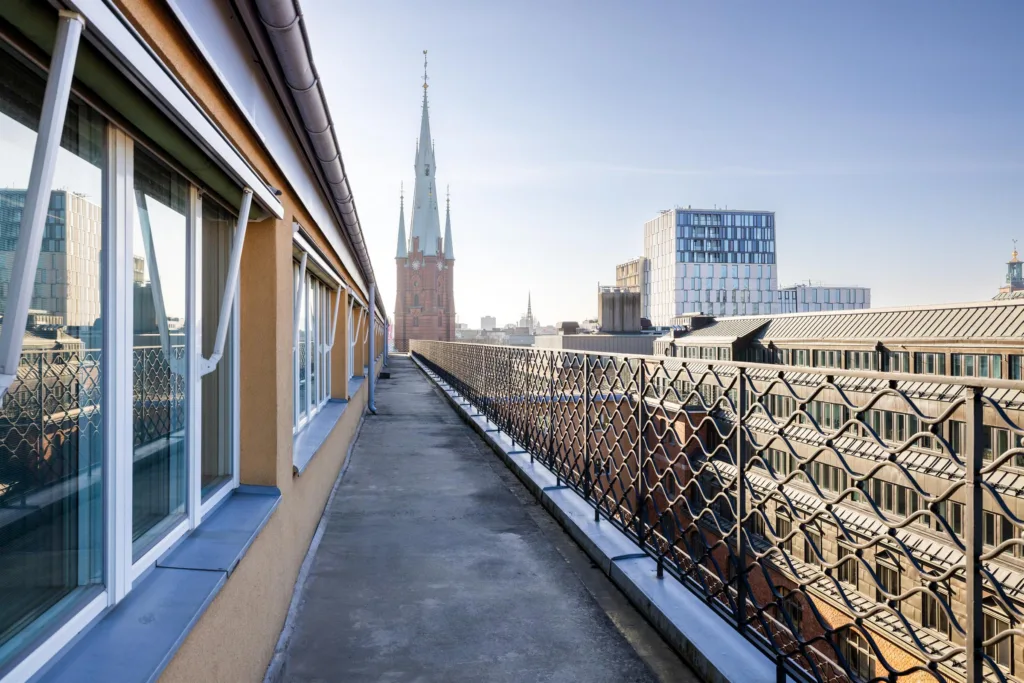 En takterrass med utsikt över stadens byggnader, inklusive en spetsig kyrka och moderna fasader.