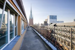 En takterrass med utsikt över stadens byggnader, inklusive en spetsig kyrka och moderna fasader.