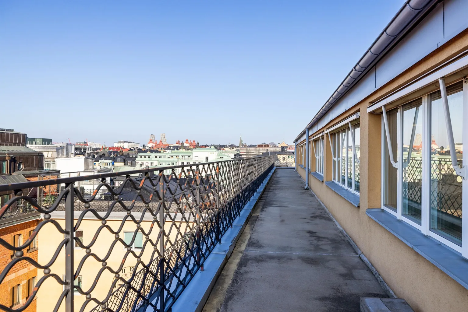 En lång takterrass med skyddsnät och utsikt över stadens byggnader under en klar blå himmel.