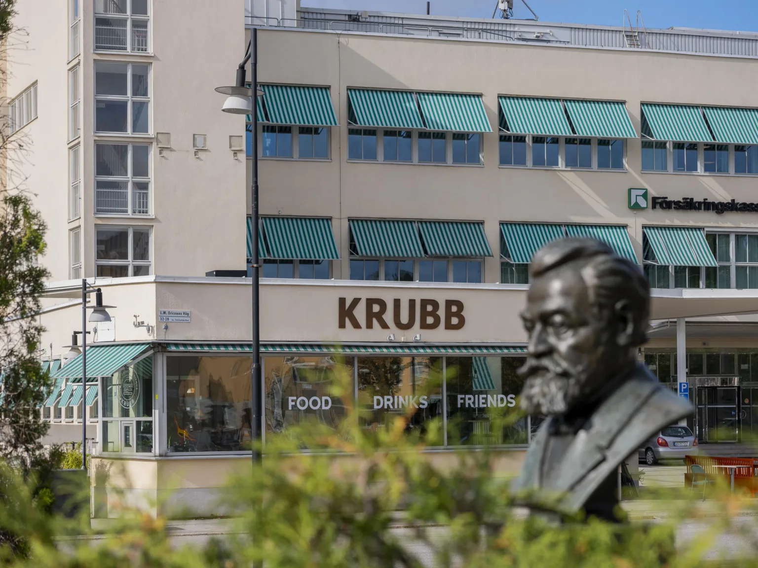 En byggnad med texten "KRUBB" på fasaden, samt en bronsbyst i förgrunden.