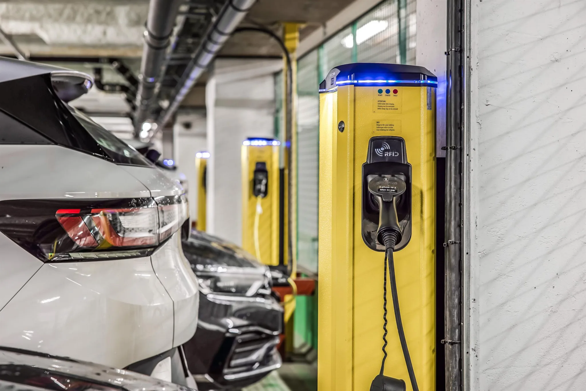 1. En gul laddstation för elbilar i en parkeringsgarage, med flera parkerade bilar i bakgrunden.