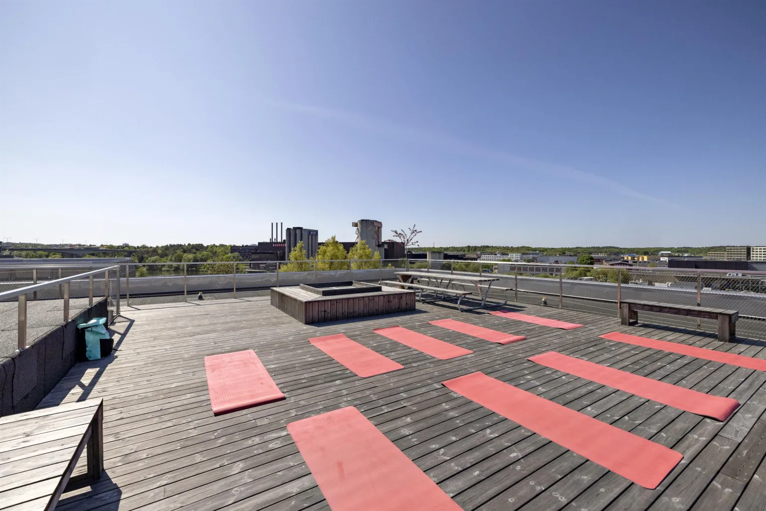 En takterrass med röda yogamattor, utsikt över staden och blå himmel.