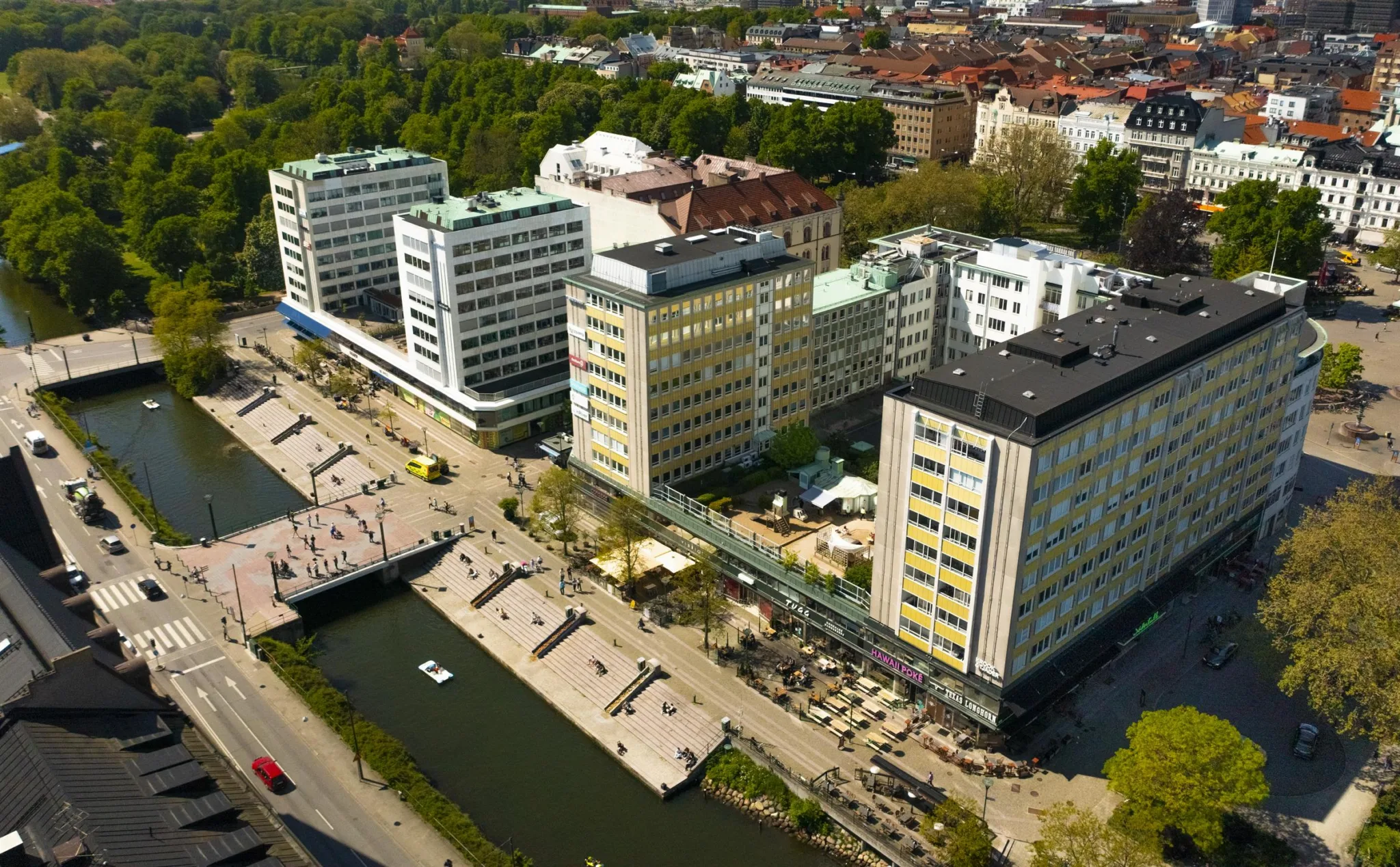 4. Flygfoto över flera kontorsbyggnader vid en kanal, omgiven av grönområden och stadsmiljö.