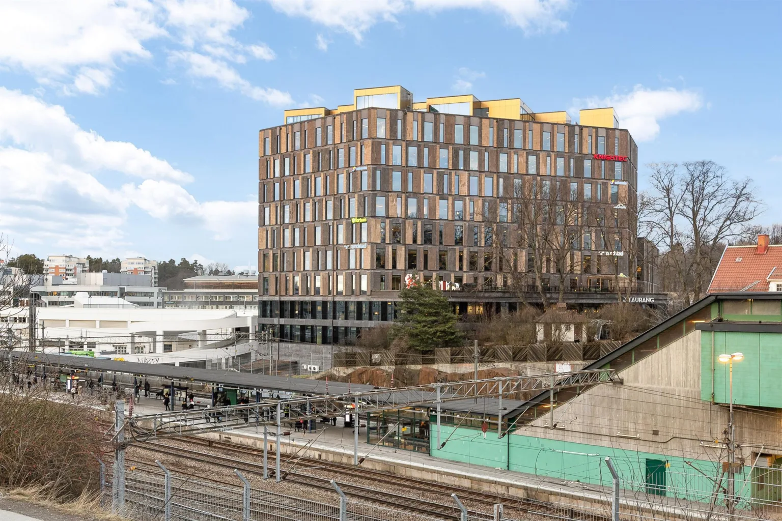 4. En modern kontorsbyggnad med träfasad och färgglada detaljer, omgiven av tågspår.