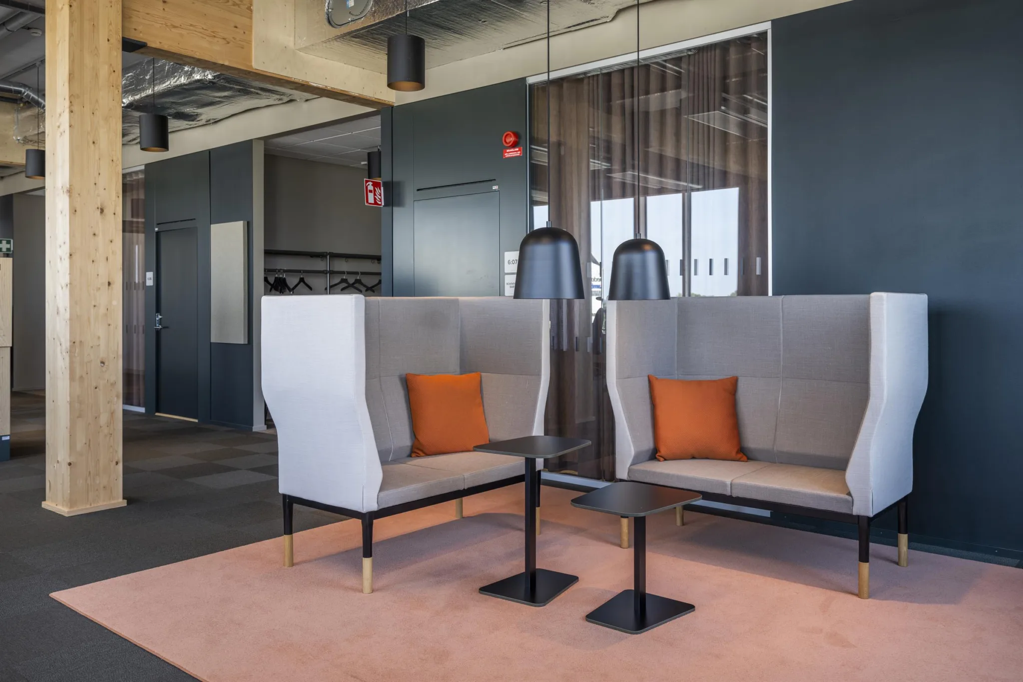 5. Ett loungeområde med två gråa soffbås, orange kuddar och små svarta bord, inrett med en modern design.