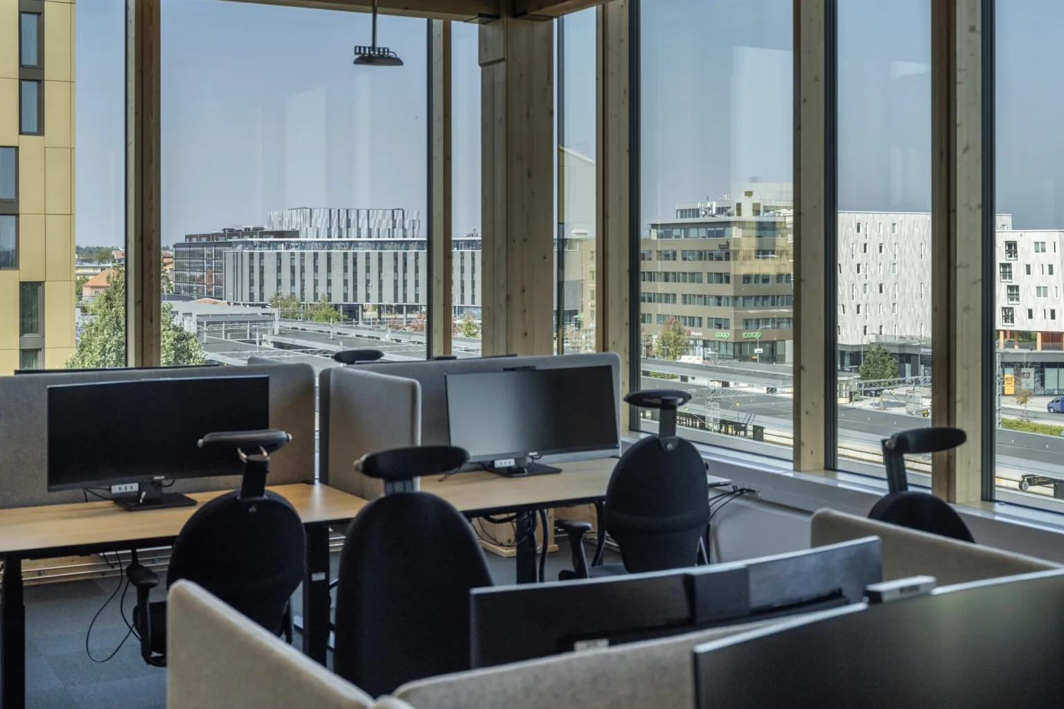5. Kontorsarbetsplatser med datorer och stolar, omgivna av stora fönster med utsikt över moderna byggnader.